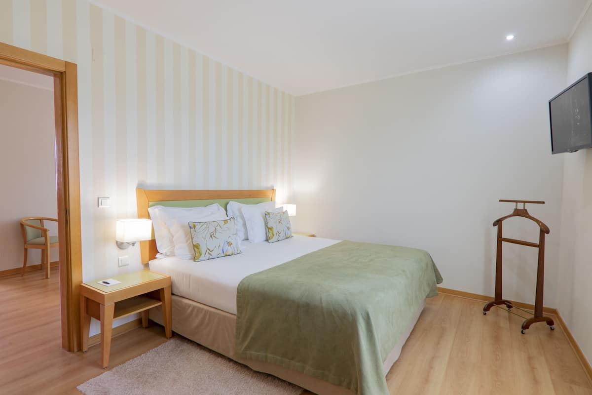 A hotel room with a bed, bedside table, lamp, and a TV mounted on the wall.