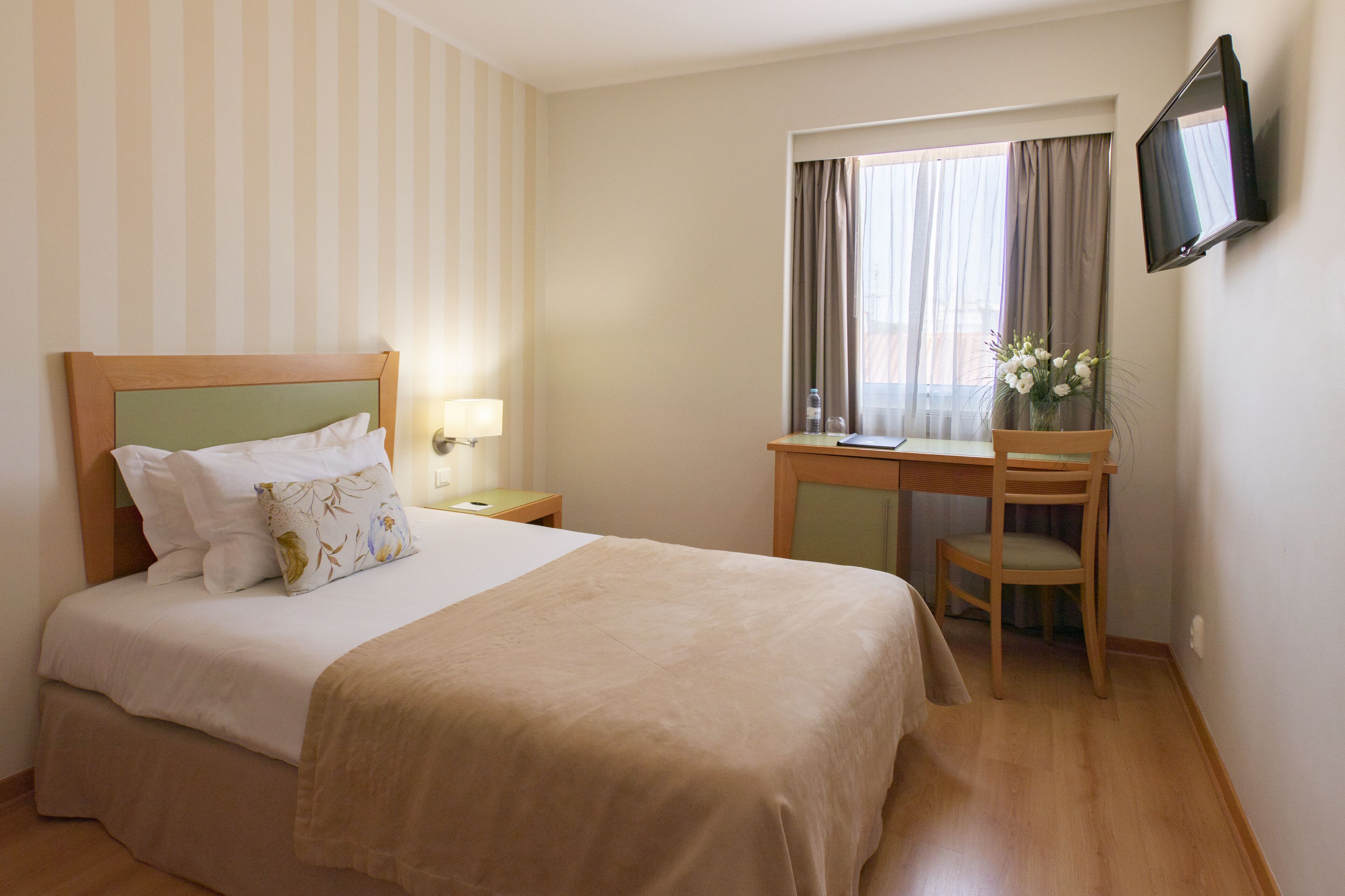 Ein Hotelzimmer mit Bett, Schreibtisch, Stuhl, Fernseher und einem Fenster mit Vorhängen.