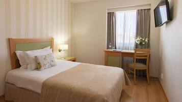 Ein Hotelzimmer mit Bett, Schreibtisch, Stuhl, Fernseher und einem Fenster mit Vorhängen.