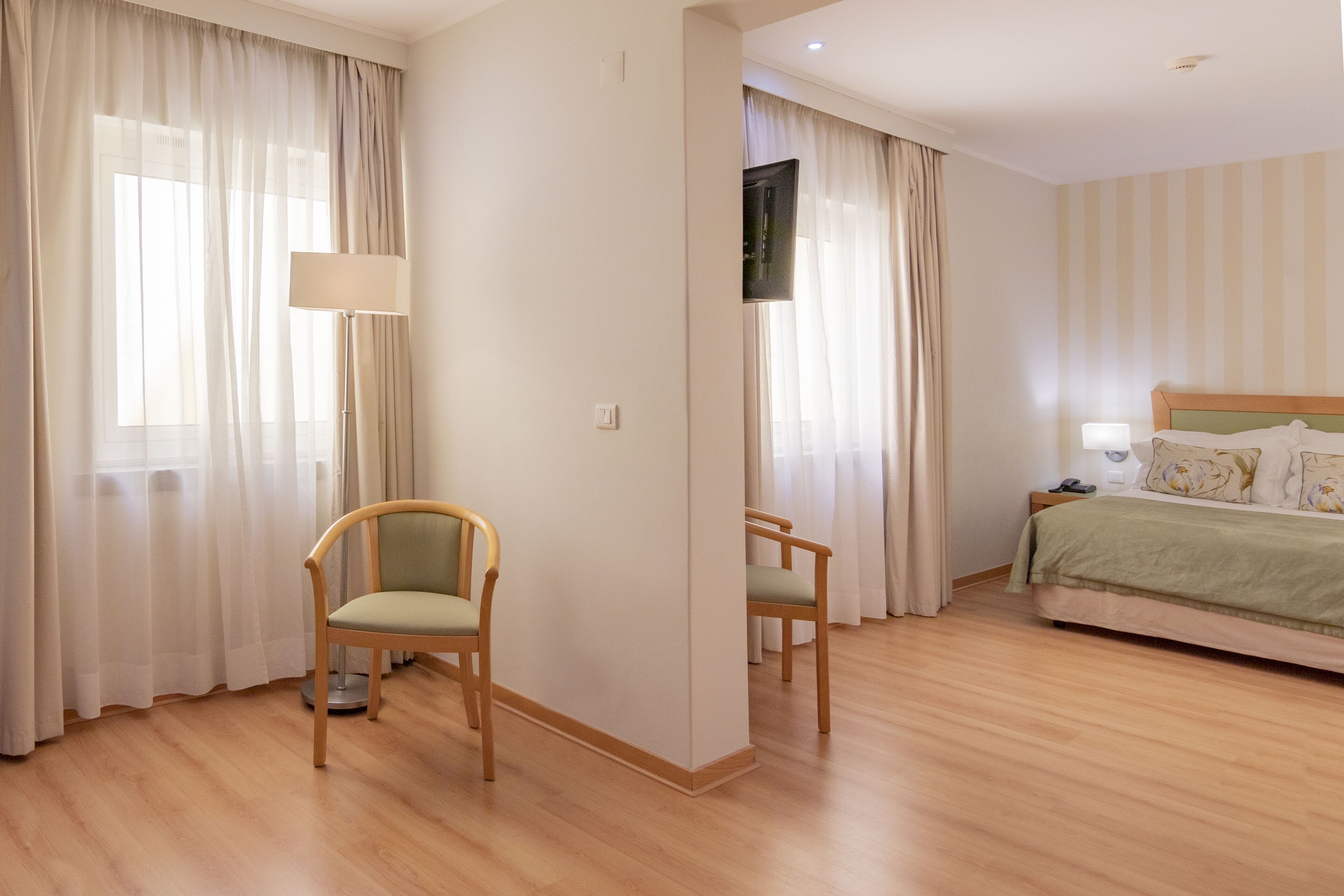 Une chambre d’hôtel avec un lit, deux chaises, une lampe et des rideaux.