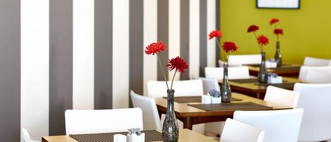 A restaurant with white chairs and tables, some with vases of red flowers.