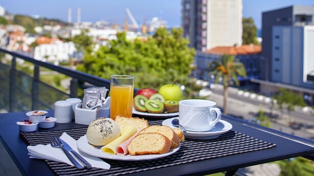 Desayuno en un balcón con vista a la ciudad, que incluye un plato con pan, fruta y una taza.