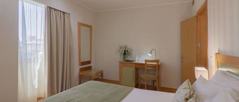 Una habitación de hotel con cama, escritorio, silla, espejo y ventana con cortinas.