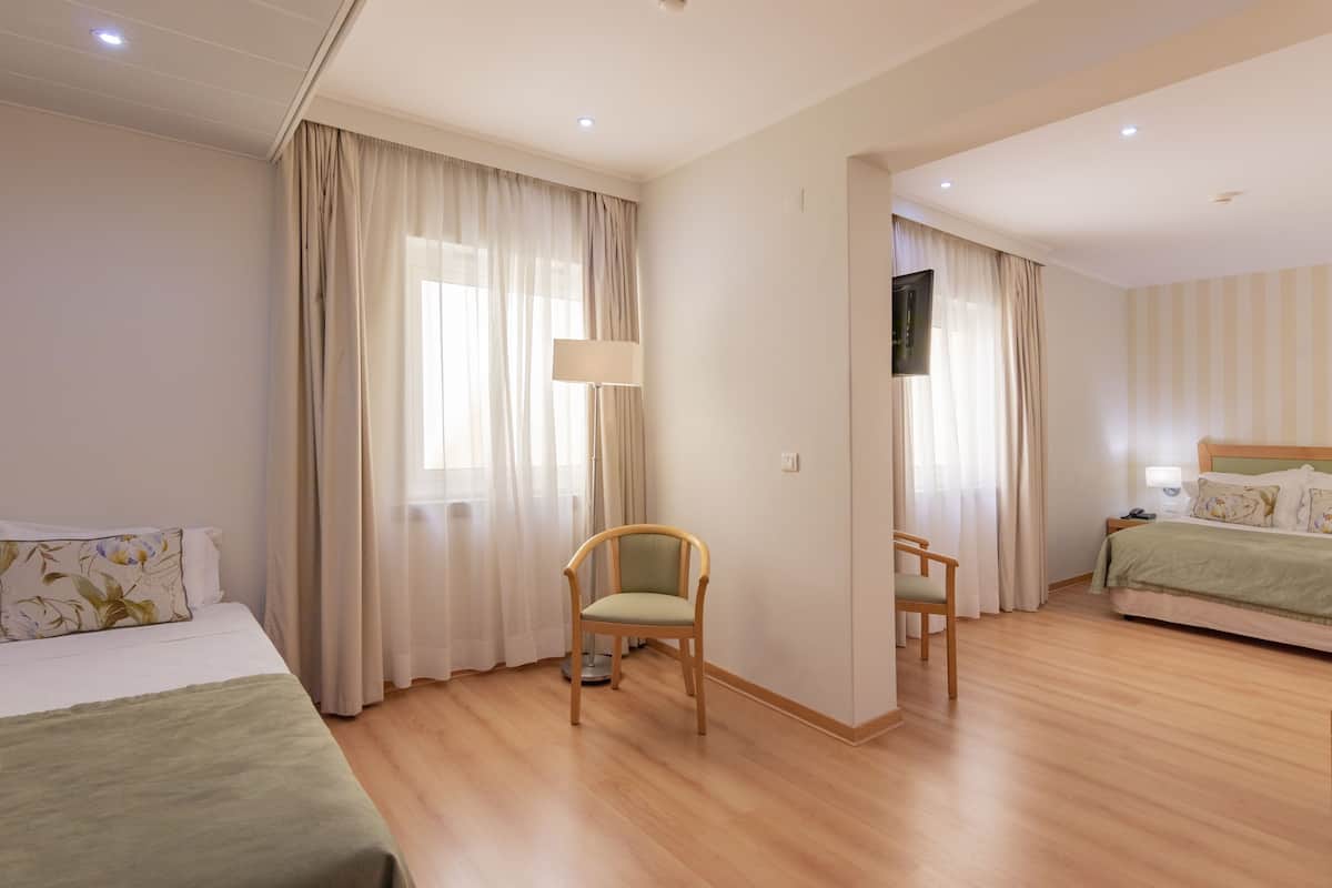A hotel room with two beds, a chair, a TV, and a lamp.