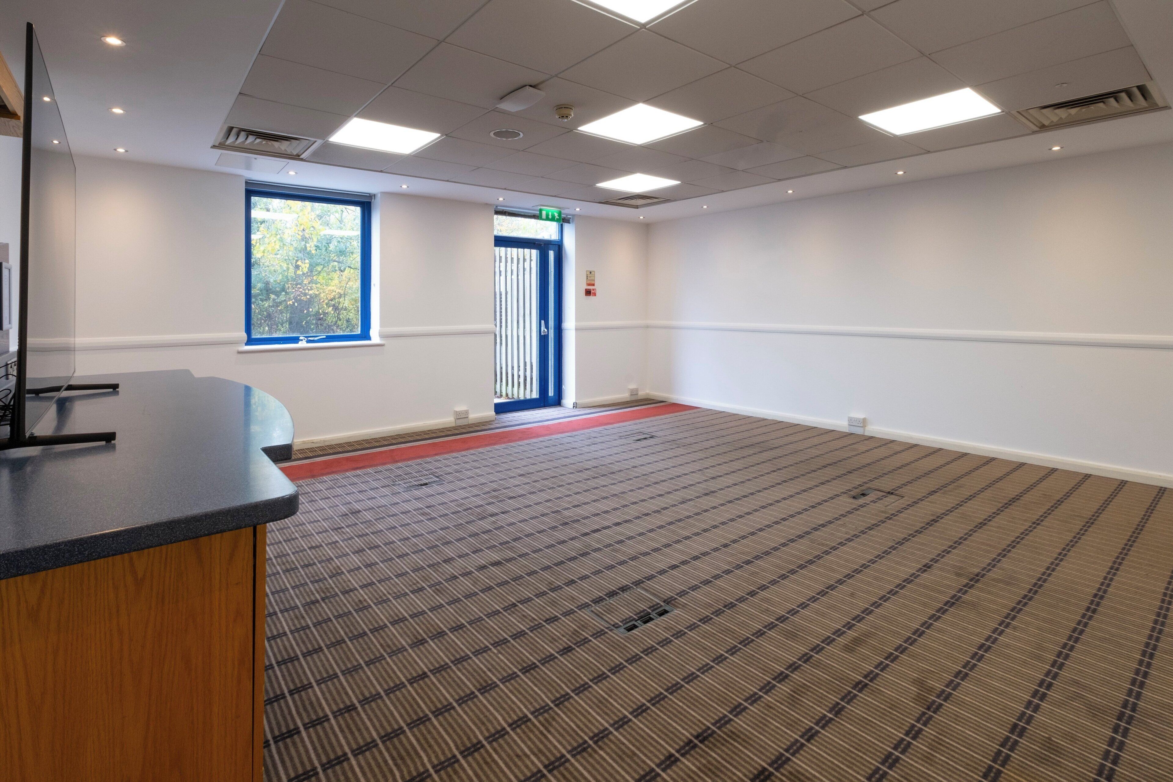 A conference room with a large window, a reception desk, and a carpeted floor.