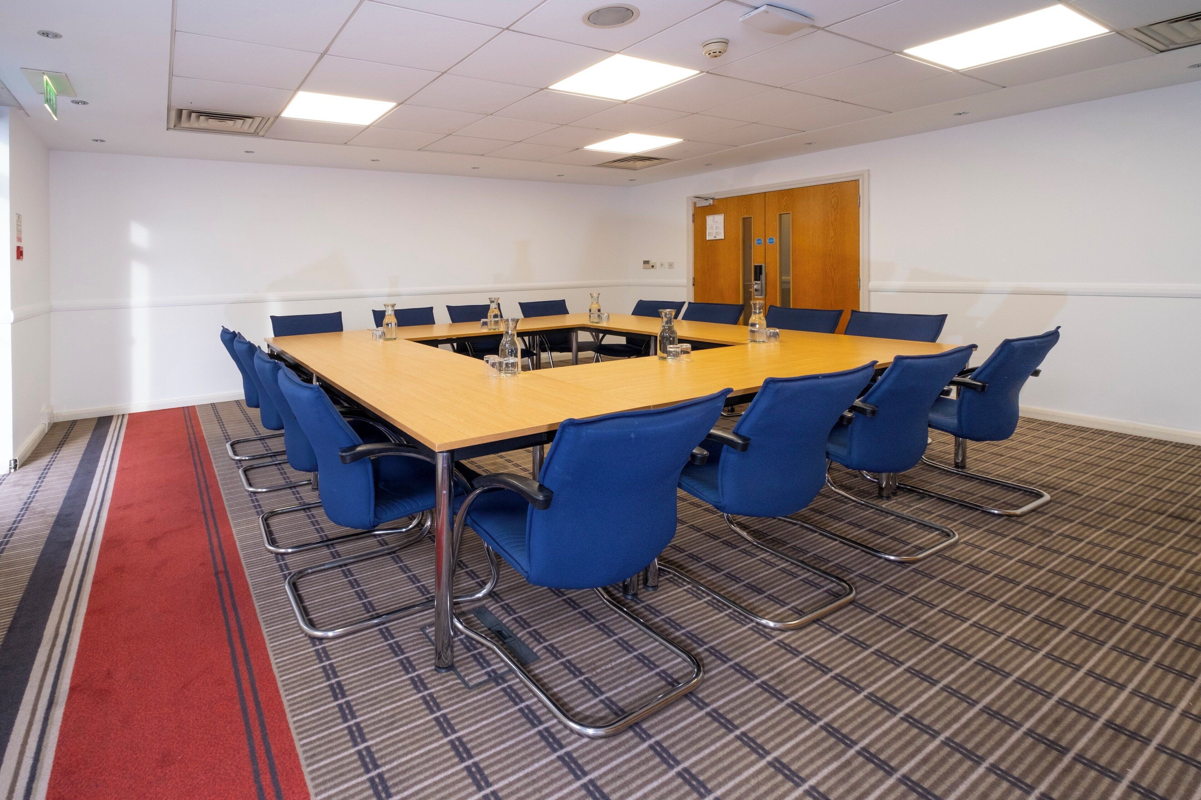 A conference room with a long table, blue chairs, and a carpeted floor.