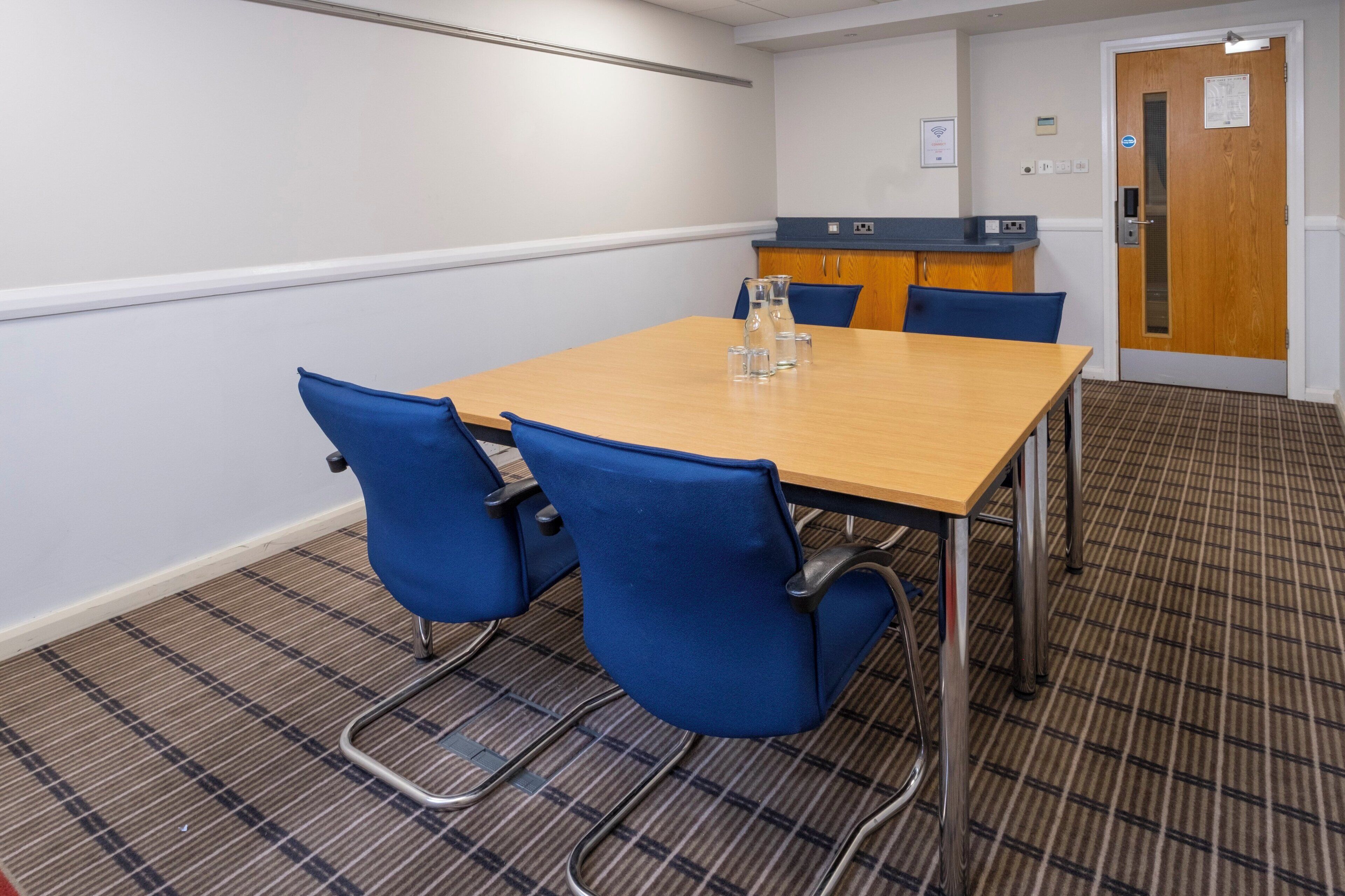 A conference room with a wooden table, blue chairs, a reception desk, and a door with a sign.