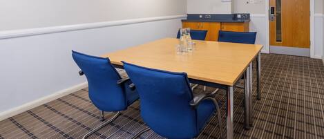 A conference room with a wooden table, blue chairs, a reception desk, and a door with a sign.