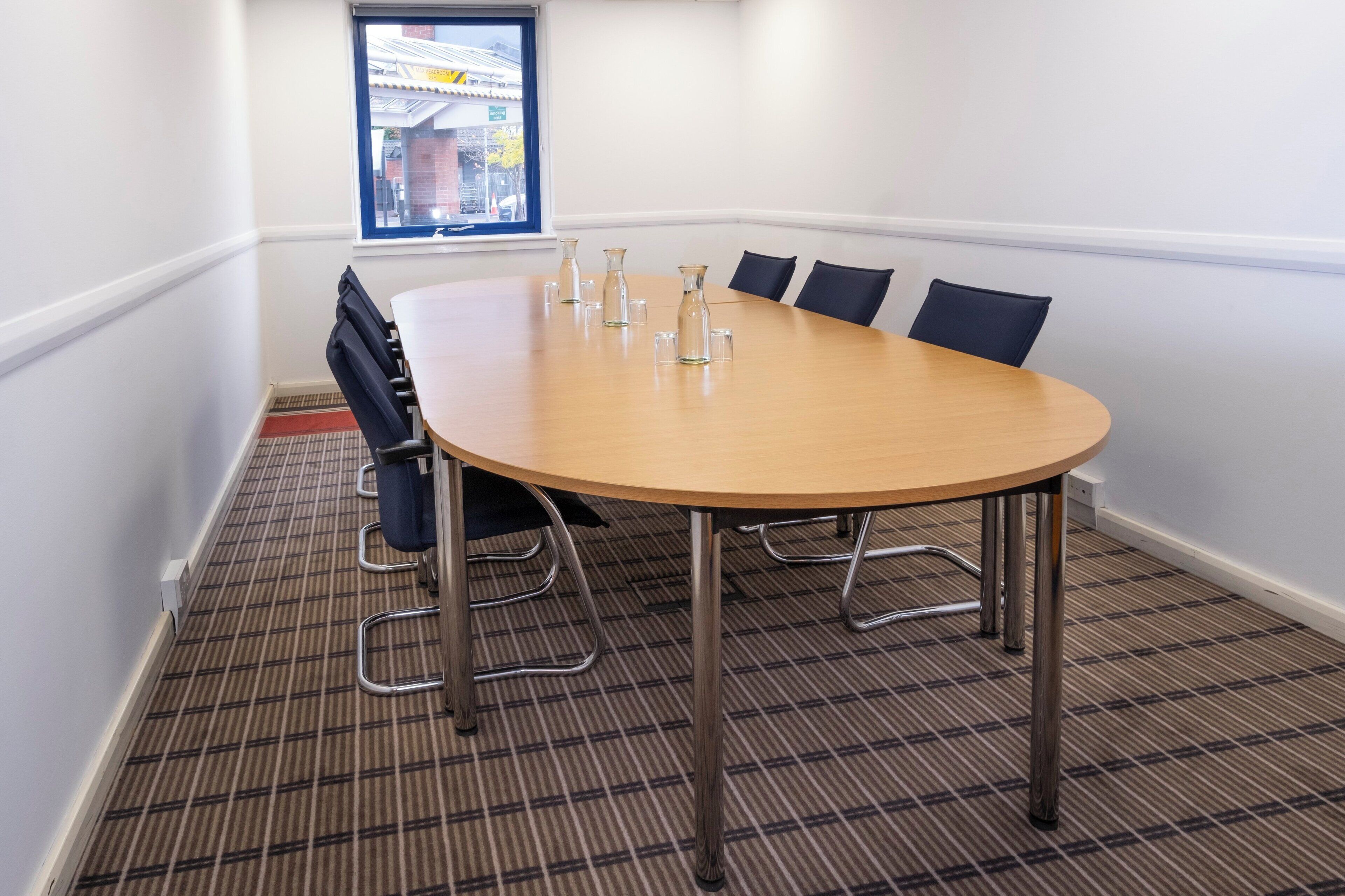 A conference room with a large oval table, six chairs, and a window with a view of buildings outside.
