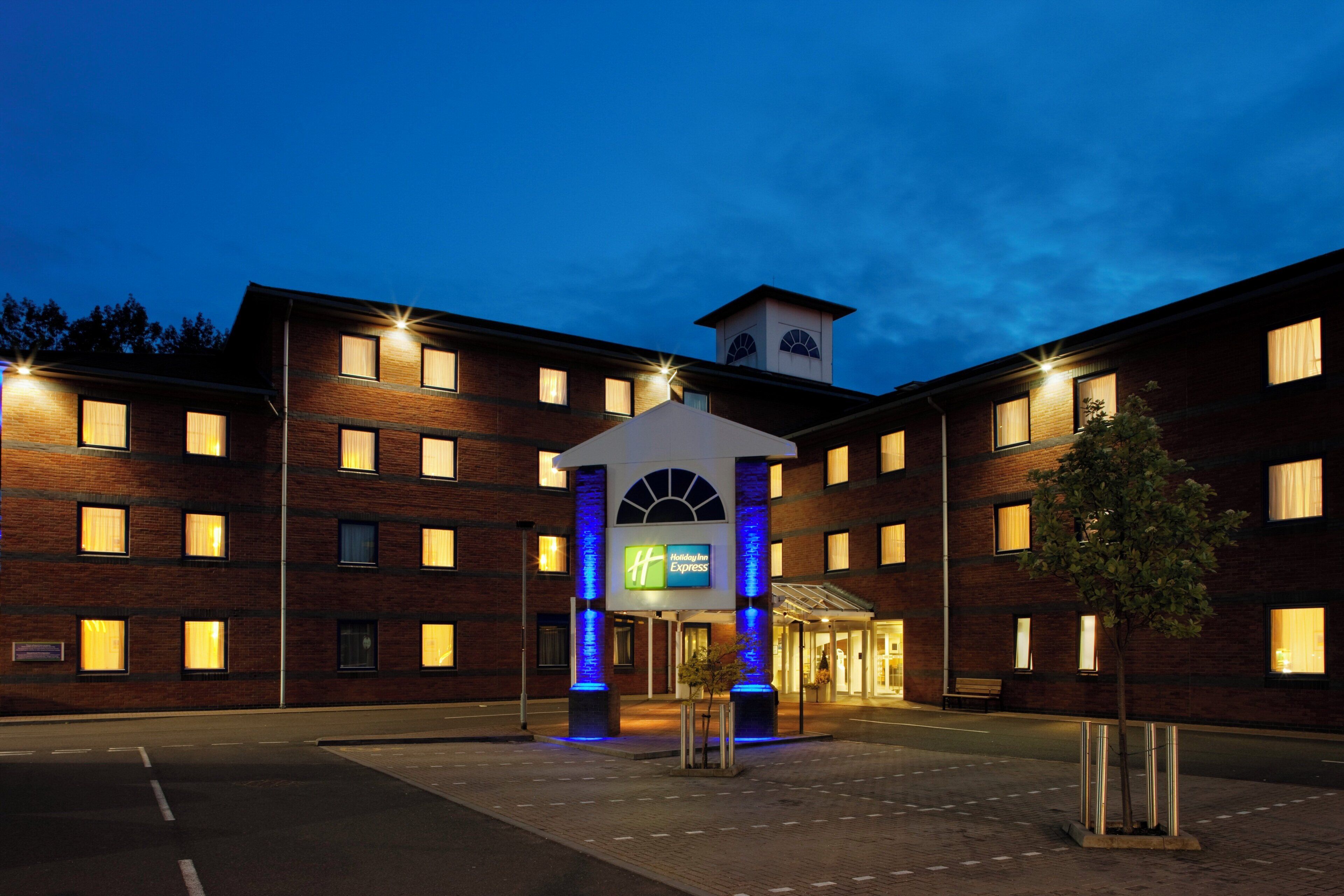 Un hotel de varios pisos con una entrada central que presenta un arco iluminado en azul y una torre del reloj.