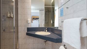 A modern bathroom with a glass shower enclosure, a sink with a dark countertop, and a towel rack with a white towel.