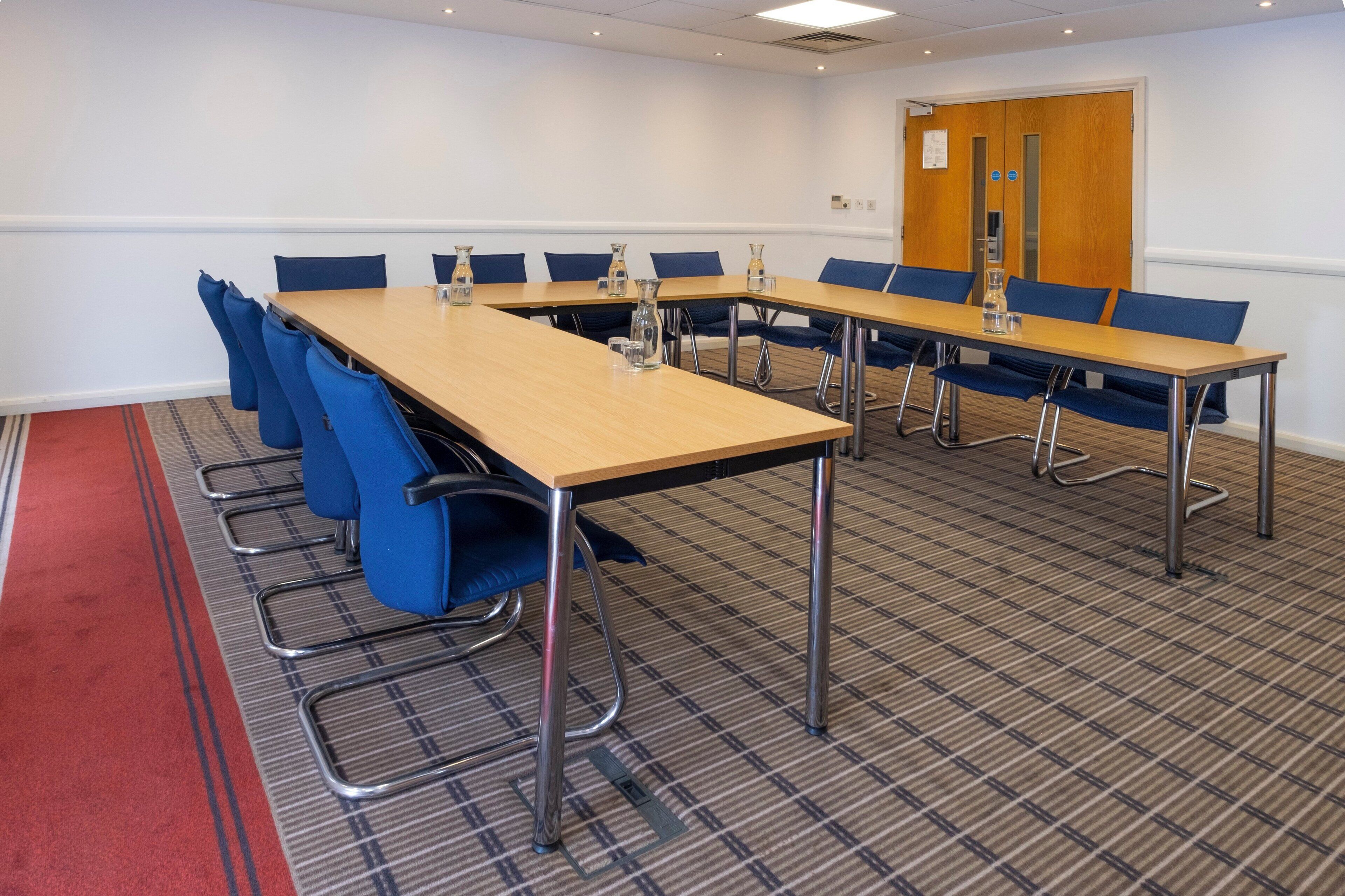 A conference room with a long table, blue chairs, and a red carpet.