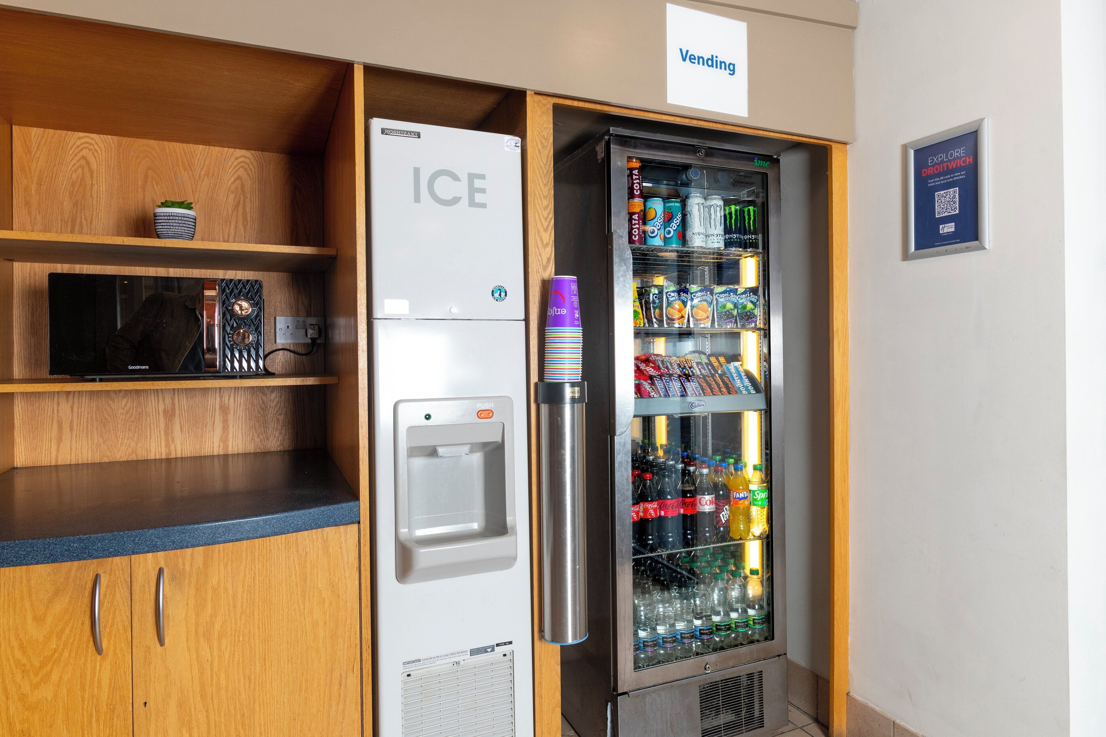 A vending machine and an ice dispenser in a room with wooden shelves and a sign indicating a vending area.