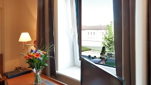 Une chambre d’hôtel équipée d’un bureau, d’une télévision, d’une télécommande, d’un plateau avec des pâtisseries et des tasses à café, et d’un vase rempli de fleurs.