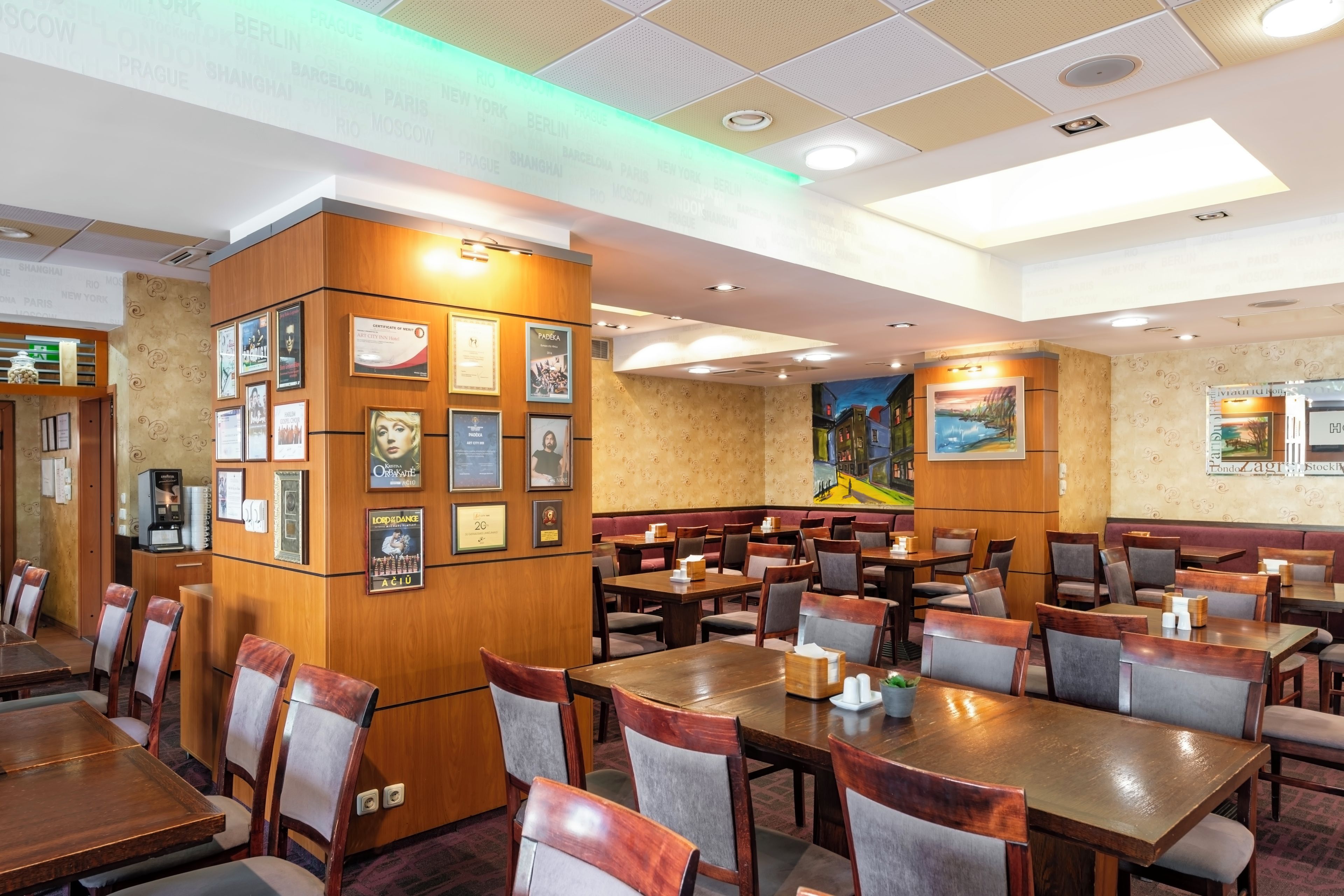 A restaurant with multiple dining tables and chairs, a coffee machine, and various framed certificates and awards on the walls.
