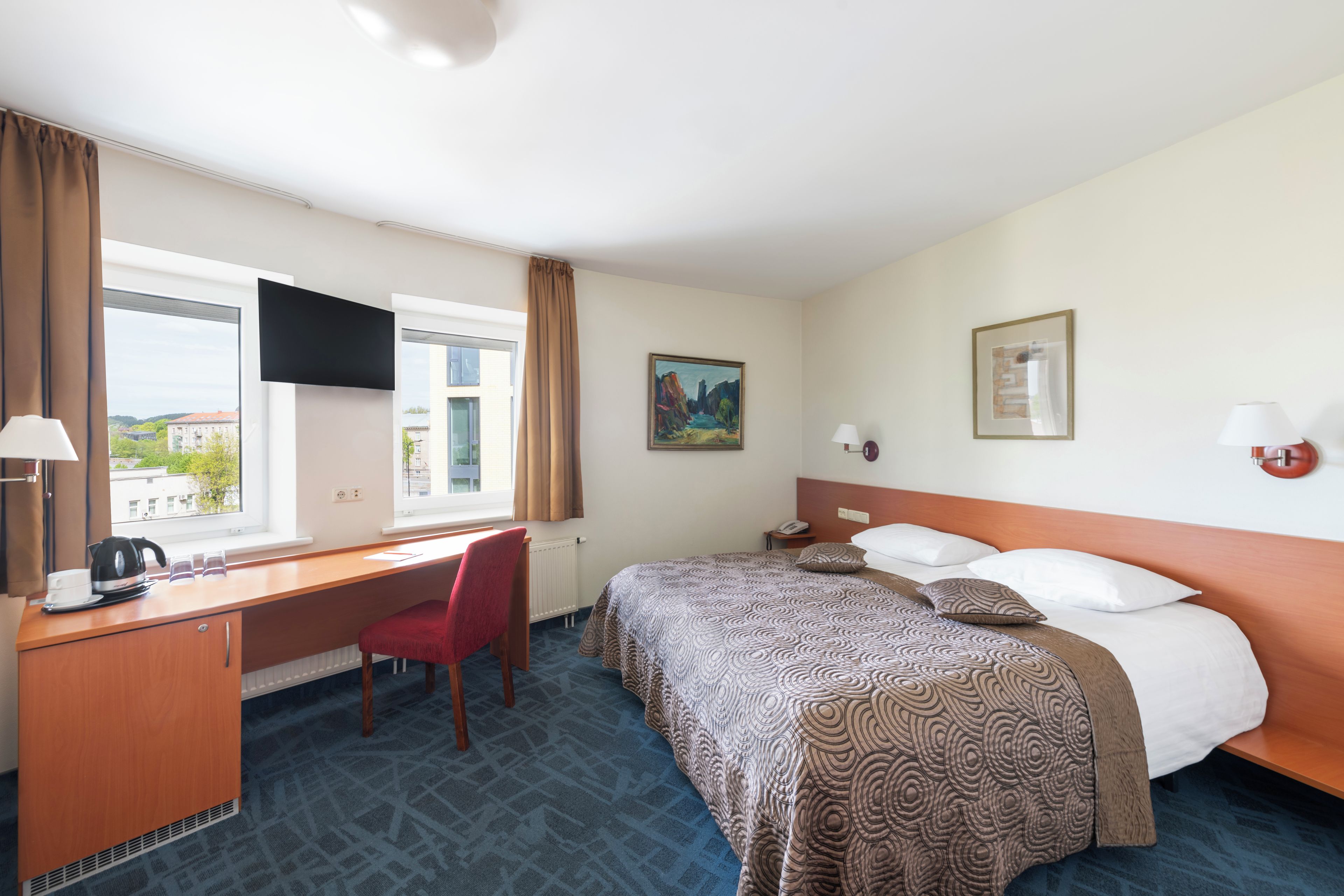 Una habitación de hotel con cama, escritorio, silla y ventana con cortinas.