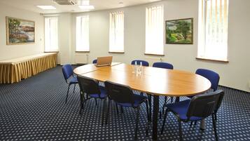A conference room with a round table, blue chairs, and two paintings on the walls.