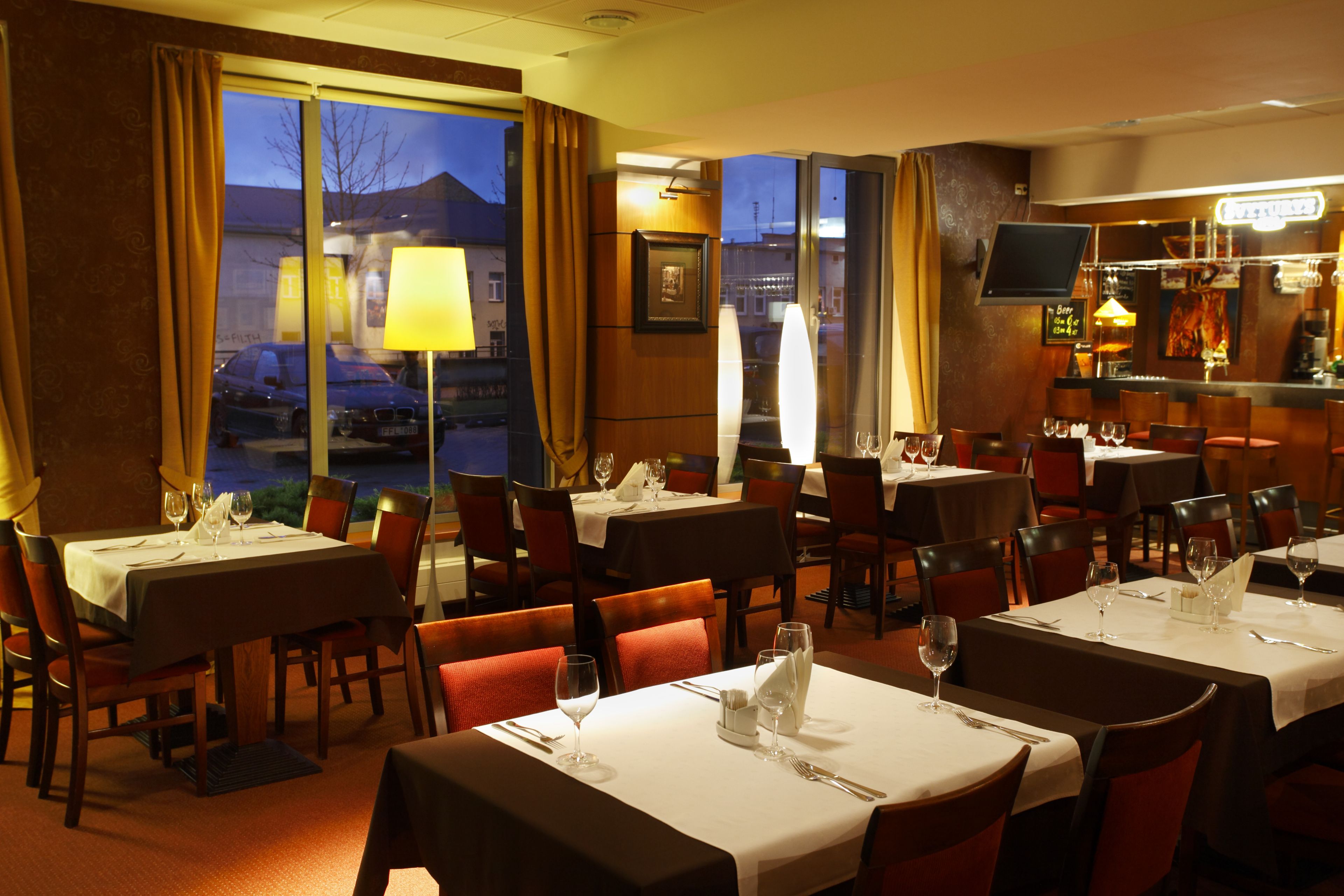 A restaurant with multiple tables set for dining, a bar area, and a view of the outside.