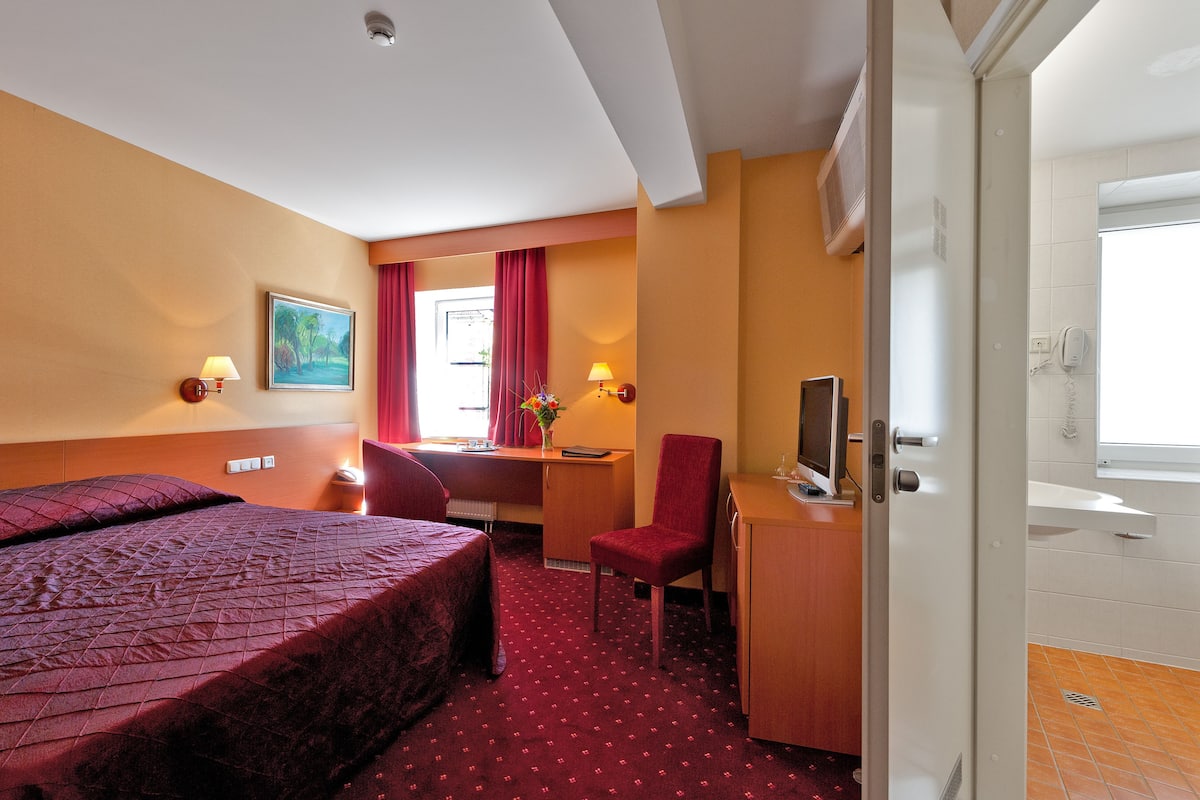 A hotel room with a bed, desk, chair, and a bathroom visible through an open door.