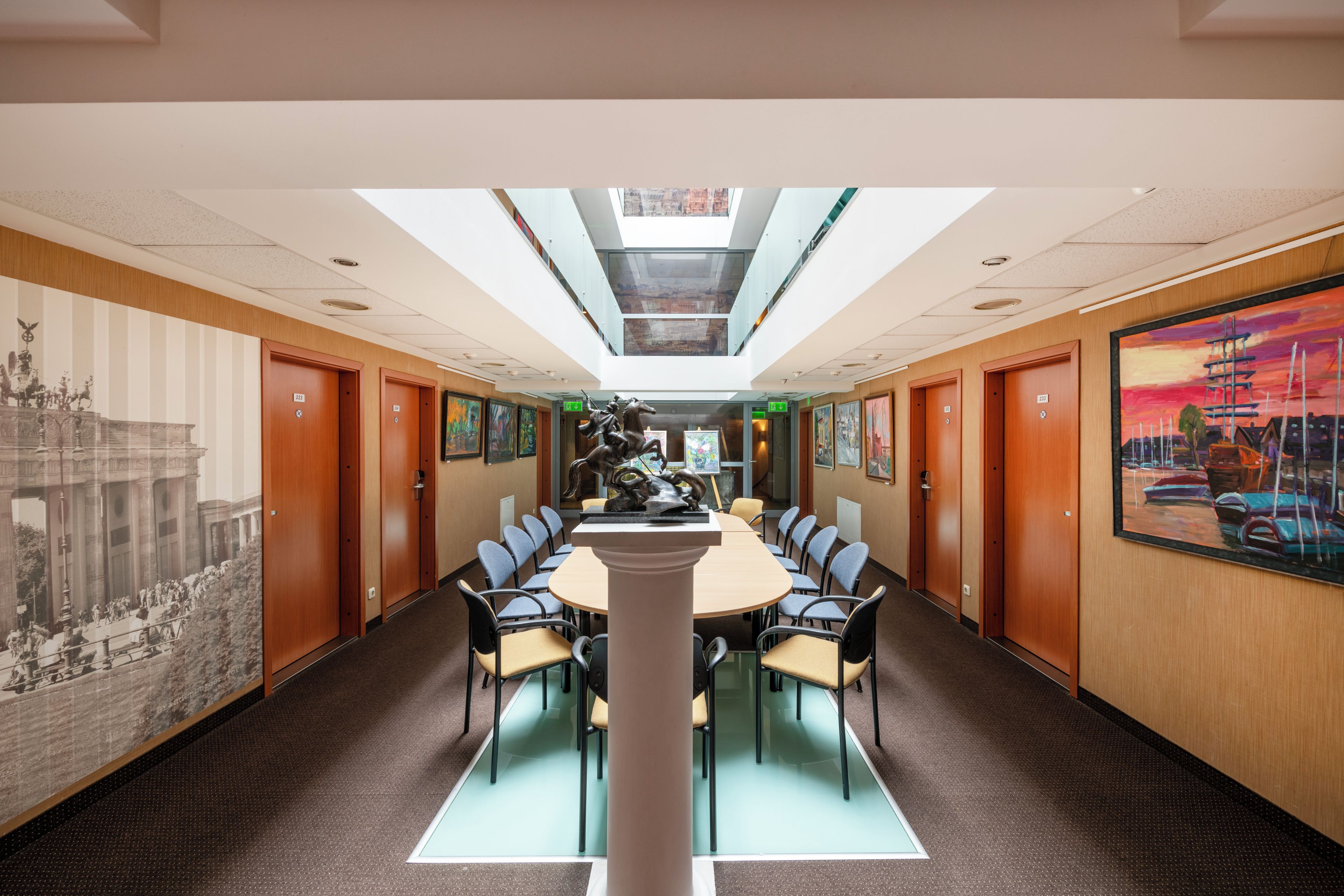 Um hall de hotel com uma mesa redonda central, cadeiras e obras de arte nas paredes.