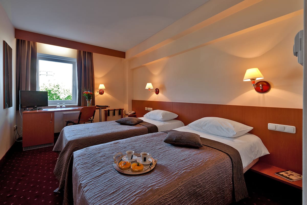 A hotel room with two beds, a desk with a computer, a chair, and a tray with breakfast items.
