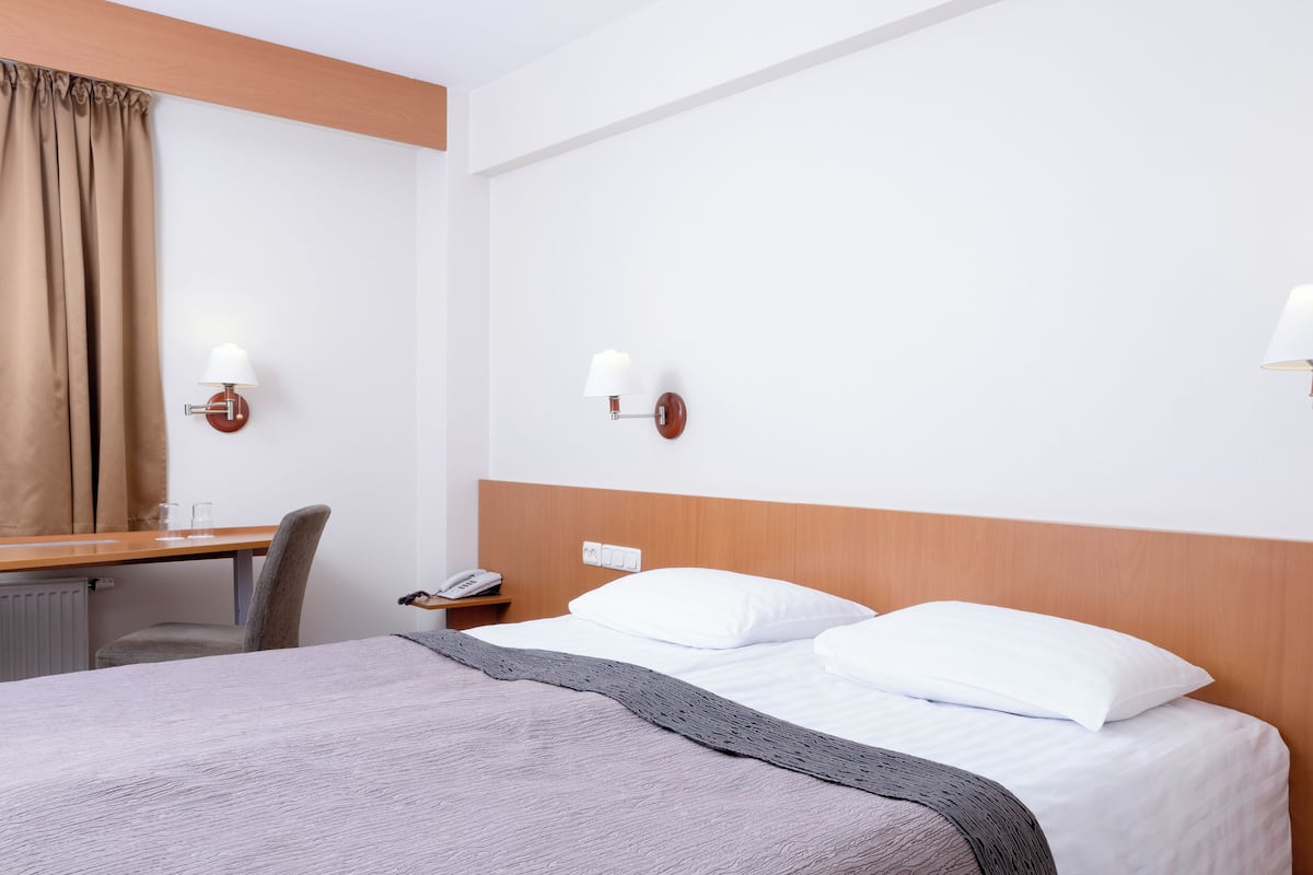Una habitación de hotel con cama, mesita de noche, lámpara y escritorio con silla.
