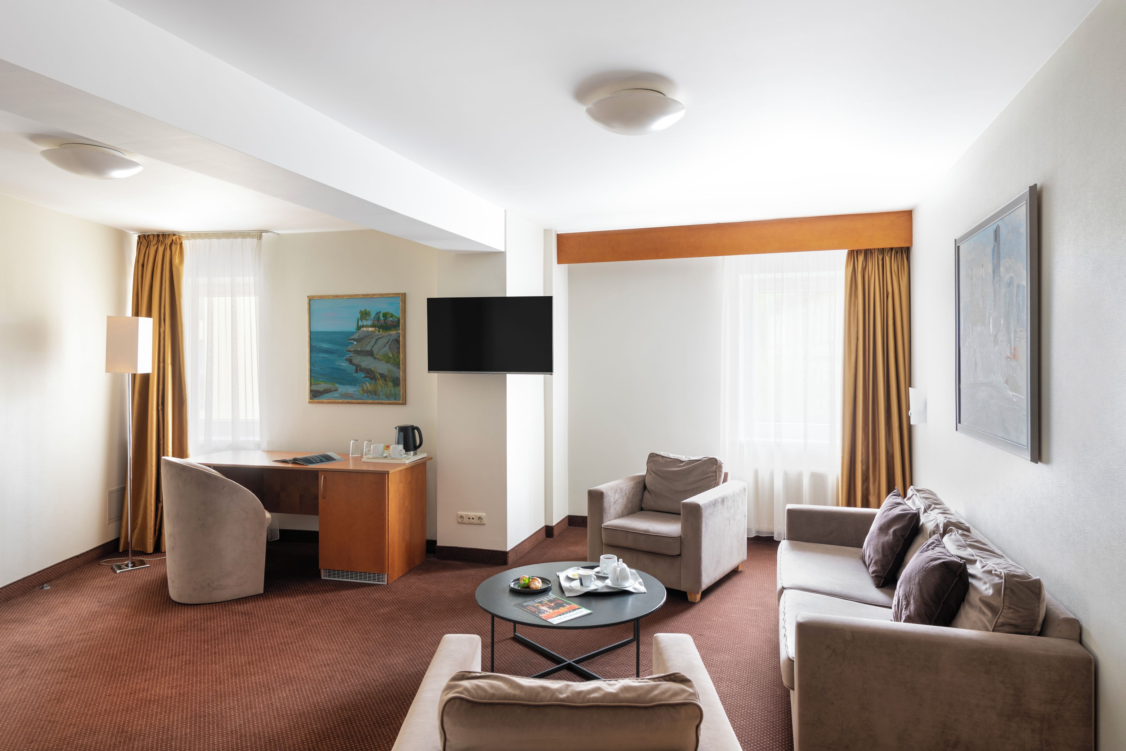 Una camera d'albergo con televisione a schermo piatto, una scrivania, due poltrone, un divano e un tavolino.