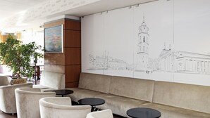 Un espace lounge moderne agrémenté d’une grande fresque murale représentant un paysage urbain, de sièges confortables et d’une grande plante.