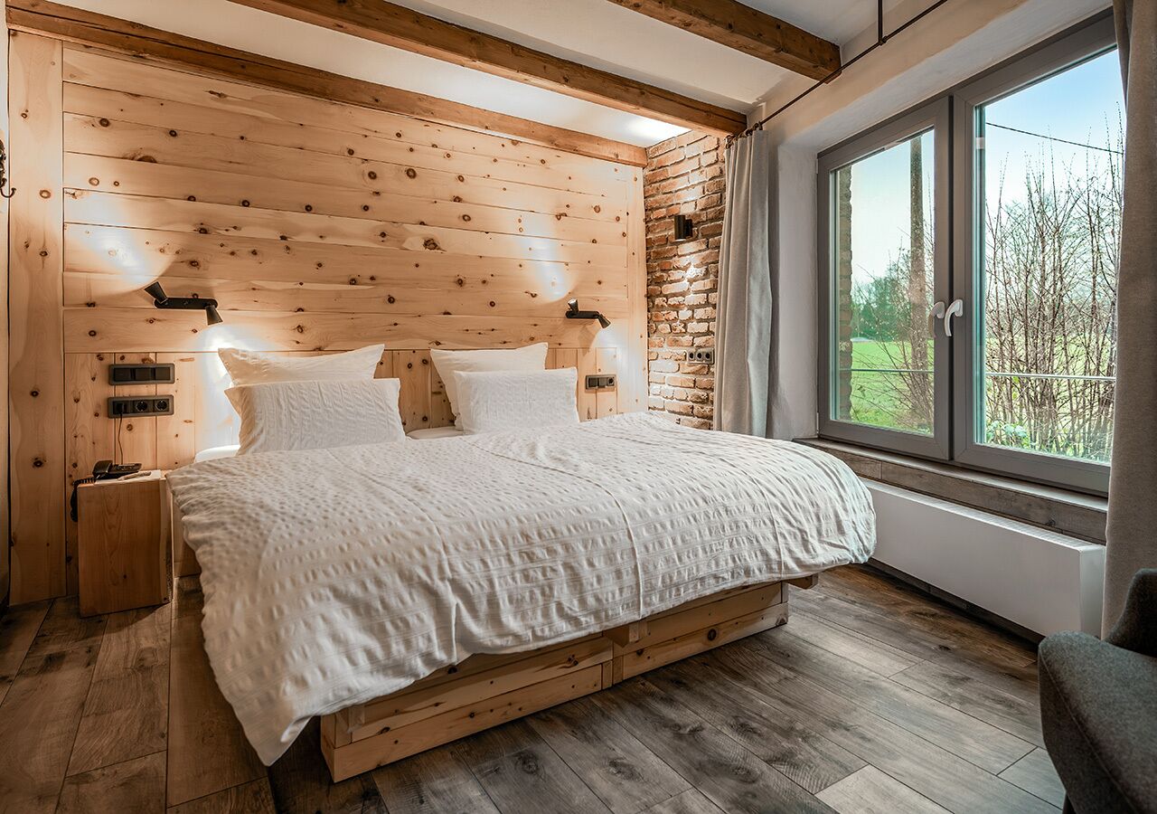 Ein Schlafzimmer mit einem Holzkopfteil, einem großen Fenster und einem Bett mit weißer Bettwäsche.