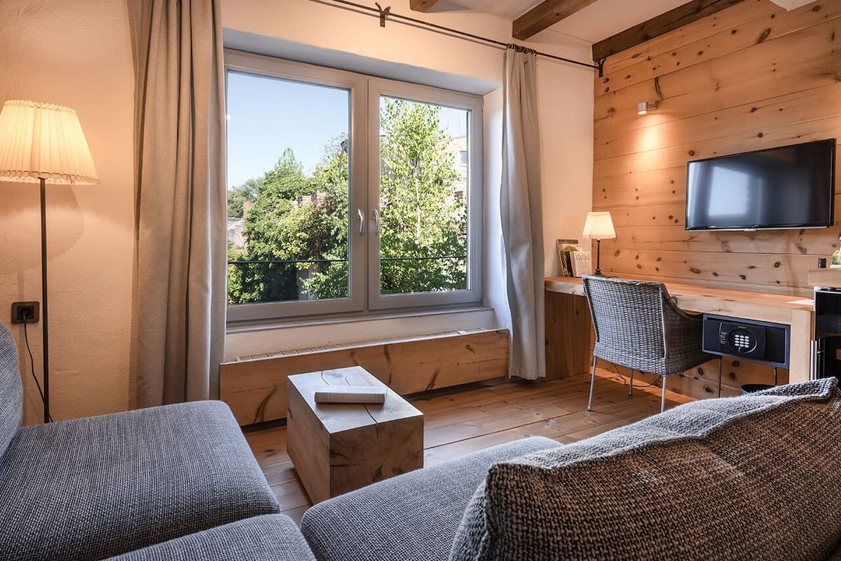 A cozy living room with a large window, a flat-screen TV, a wooden desk, and a comfortable sofa.