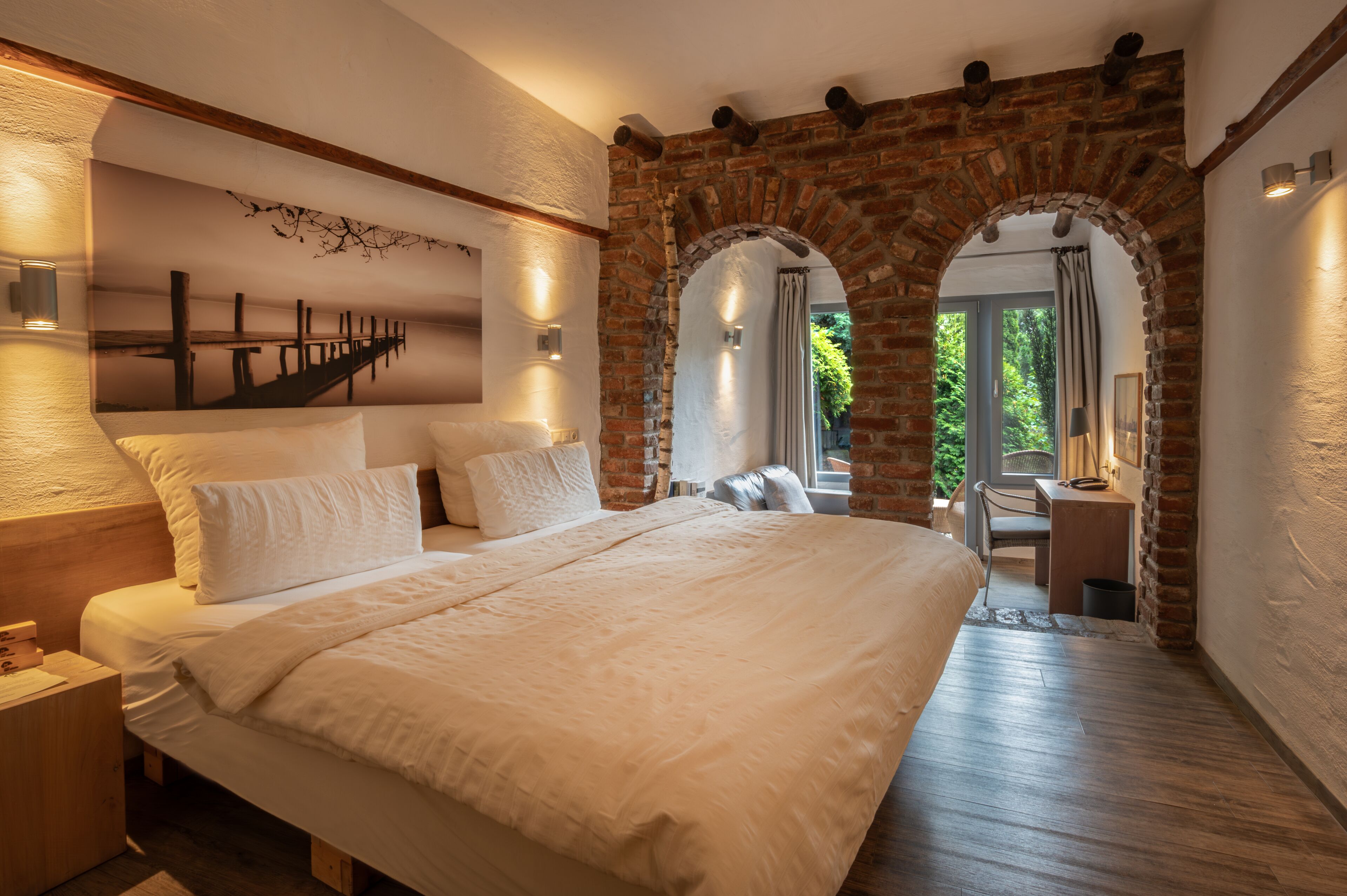 Ein geräumiges Schlafzimmer mit einem großen Bett, einem hölzernen Nachttisch, einem Schreibtisch und einem Stuhl. Es gibt zwei gewölbte Backsteinwände und ein Wandgemälde.