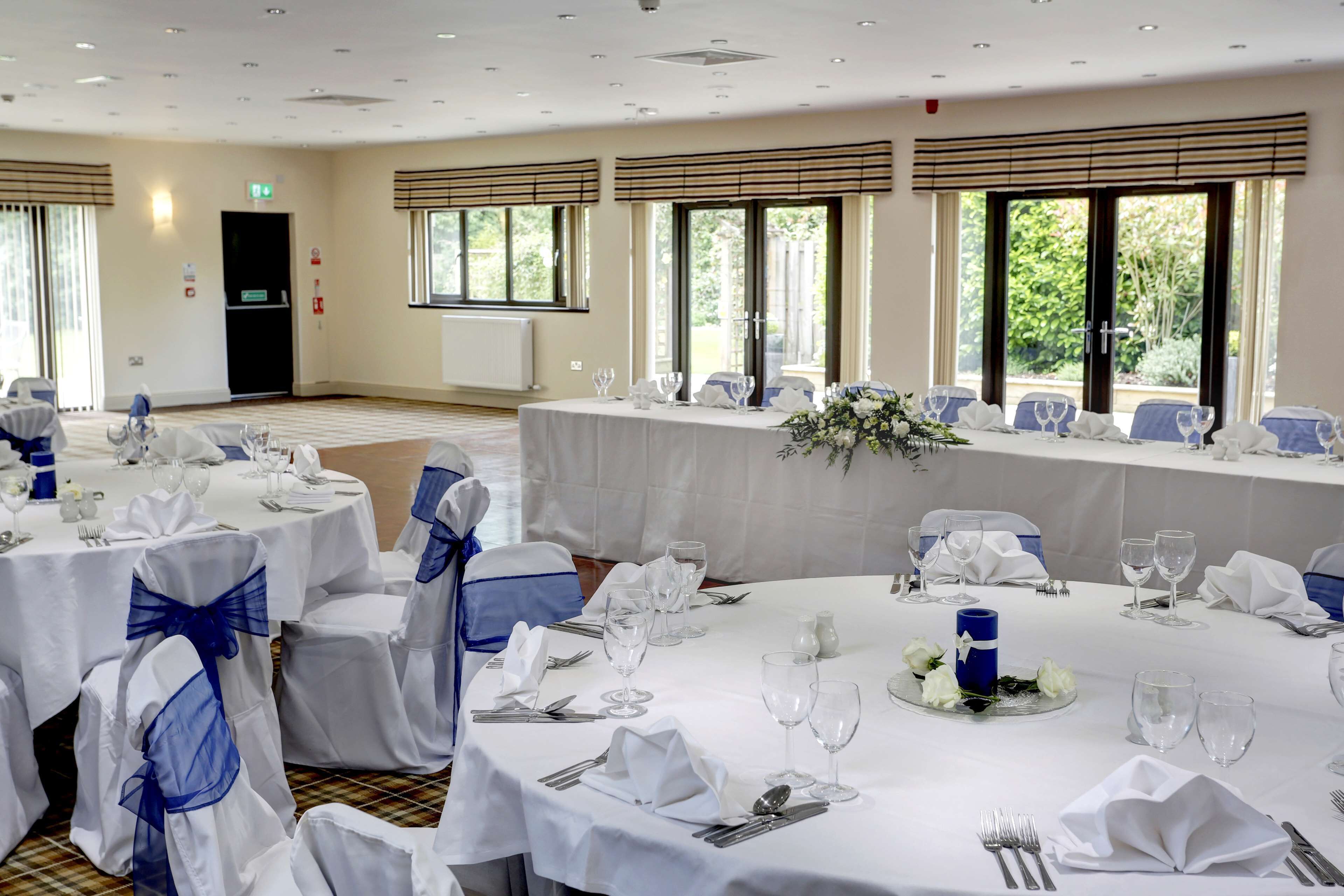 A banquet hall with round tables set for a formal event, featuring white tablecloths, blue sashes, and clear glassware.