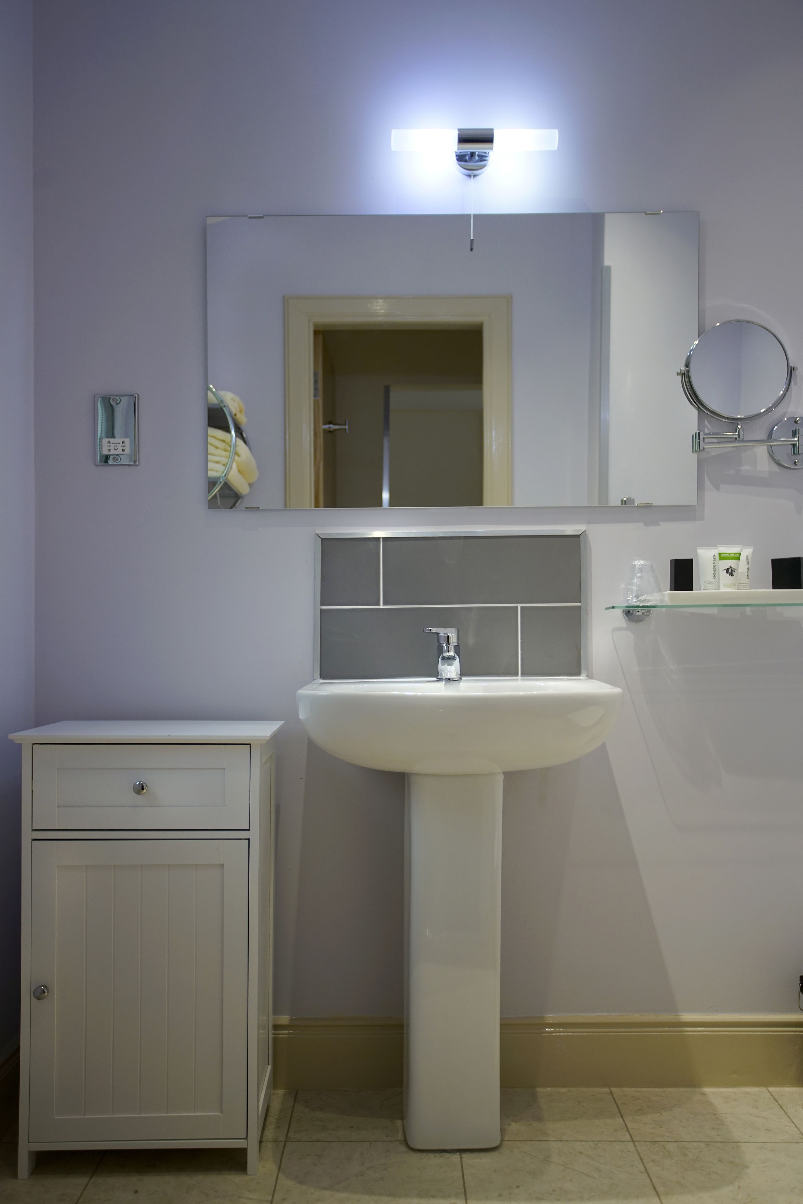 A bathroom with a white sink, a mirror, a cabinet, and a shelf with toiletries.