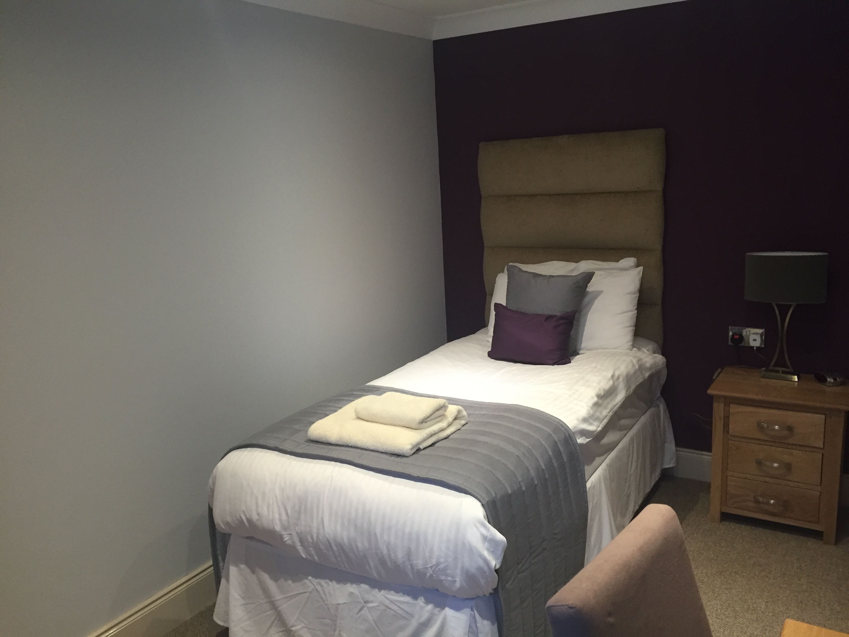 A neatly made bed with a white comforter and pillows, a bedside table with a lamp, and a wooden nightstand.
