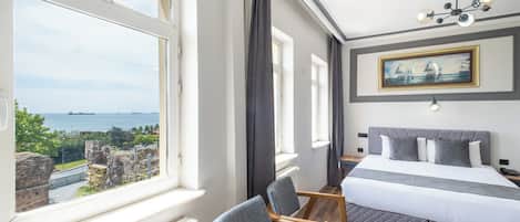 Habitación de hotel con un ventanal que ofrece vistas panorámicas, una cama con ropa de cama gris, una silla de madera y un cuadro en la pared.
