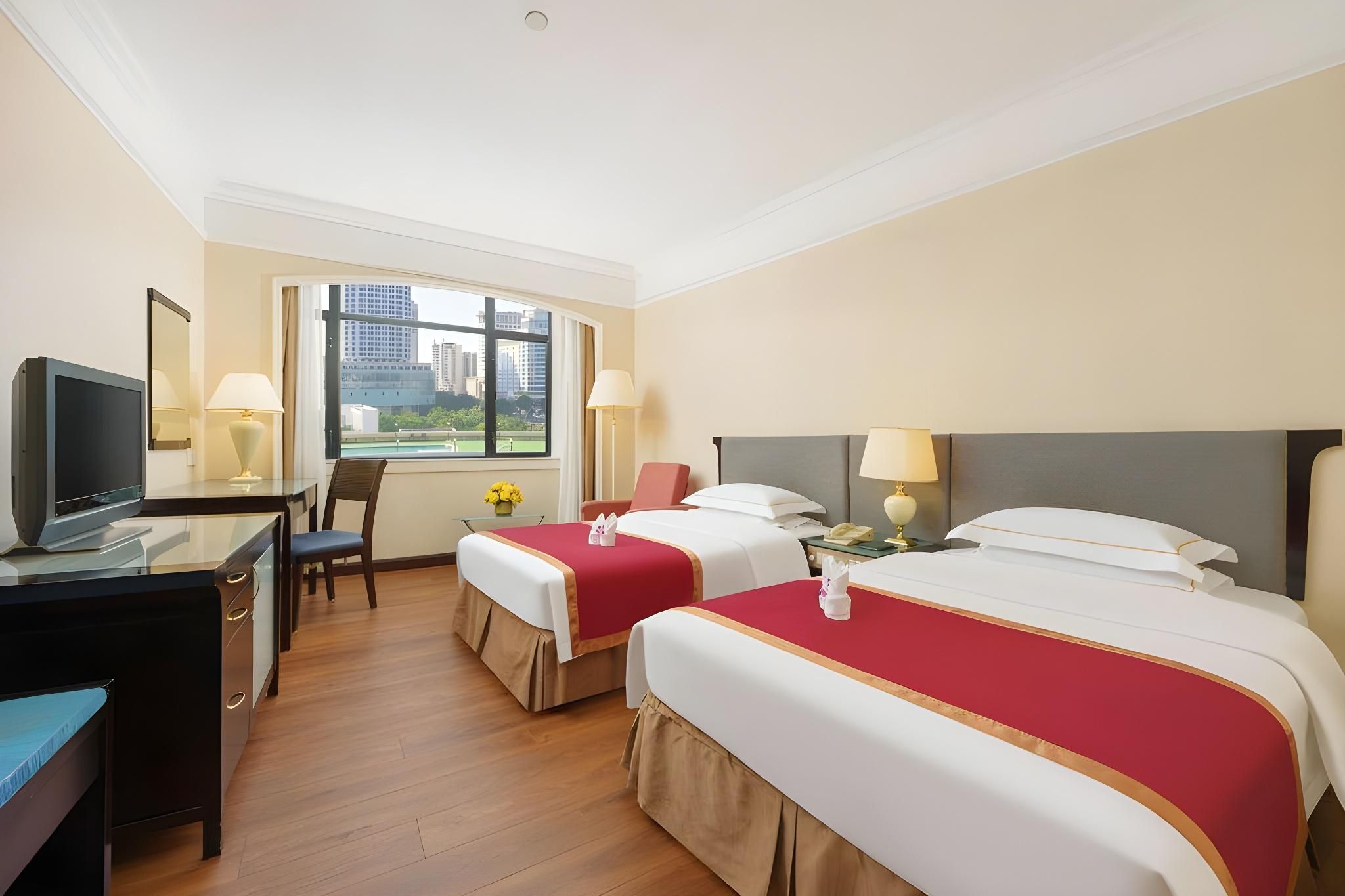 A hotel room with two beds, a desk, a chair, and a television.