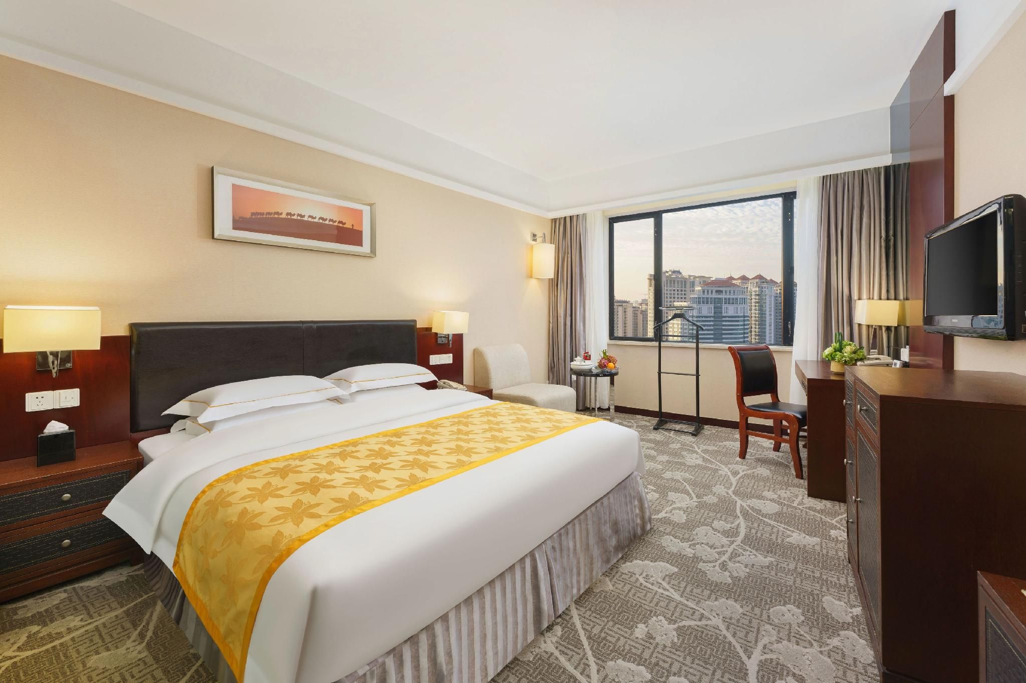 Habitación de hotel con una cama grande, un escritorio, una silla, un televisor y una ventana con vistas a la ciudad.