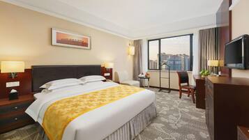 Habitación de hotel con una cama grande, un escritorio, una silla, un televisor y una ventana con vistas a la ciudad.