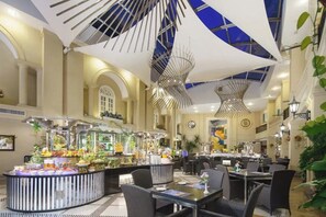 Uma sala de jantar de hotel com buffet, mesas redondas e cadeiras.