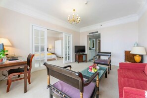 Quarto de hotel com mesa de jantar, cadeiras, sofá, televisão e lustre.