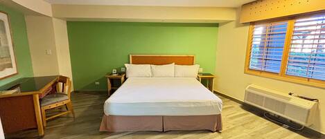 A hotel room with a wooden bed, green walls, a window with blinds, a radiator, and a chair.