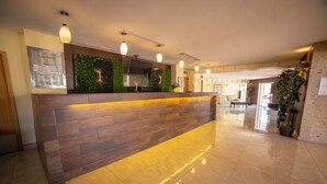 A hotel reception area with a wooden reception desk, a green wall, and a tiled floor. - Hotel Colonial Ciudad Juarez (Ciudad Juárez)