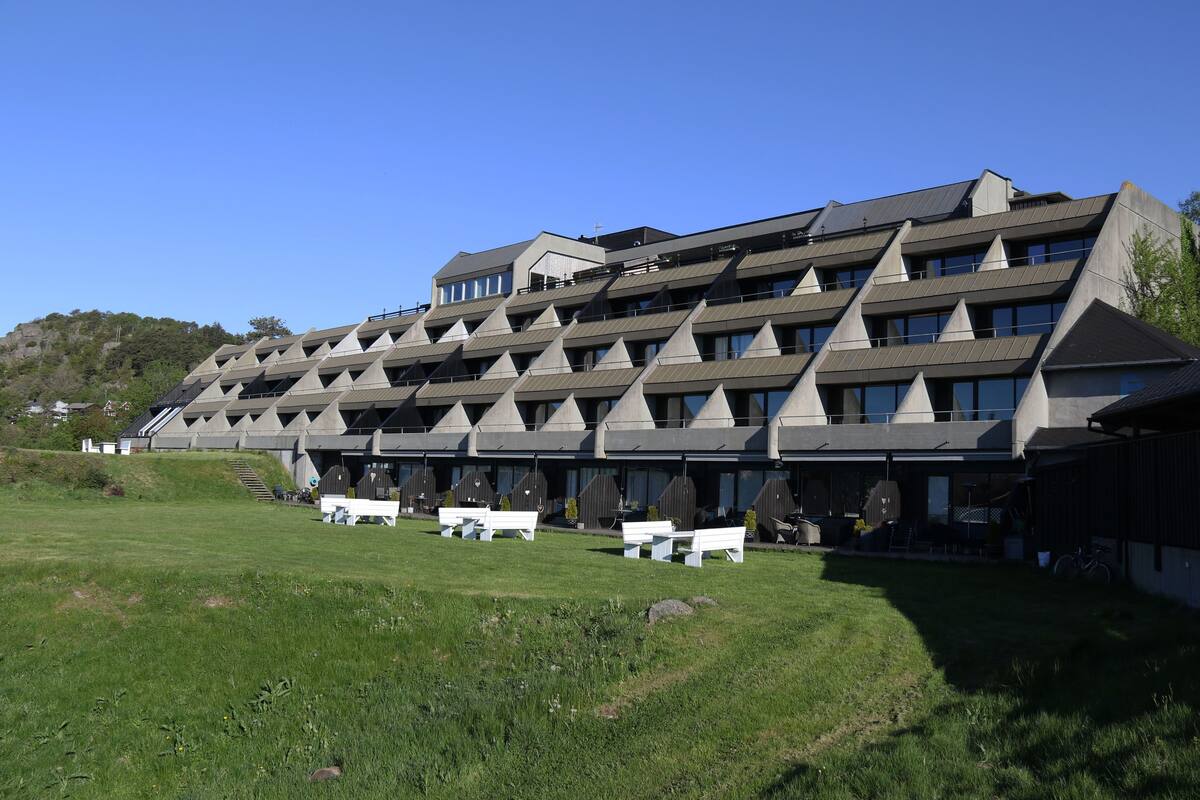 Ein modernes Gebäude mit einem markanten, dreieckigen Dach, mehreren Balkonen und Sitzgelegenheiten im Freien.