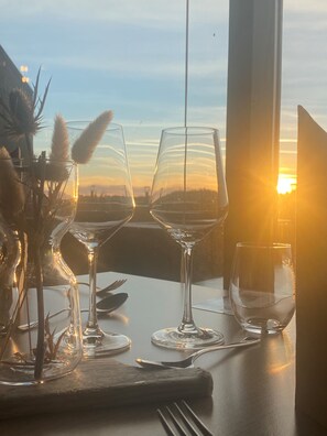 A table set for two with wine glasses and cutlery, overlooking a sunset. - Farsund Fjordhotell (Farsund)