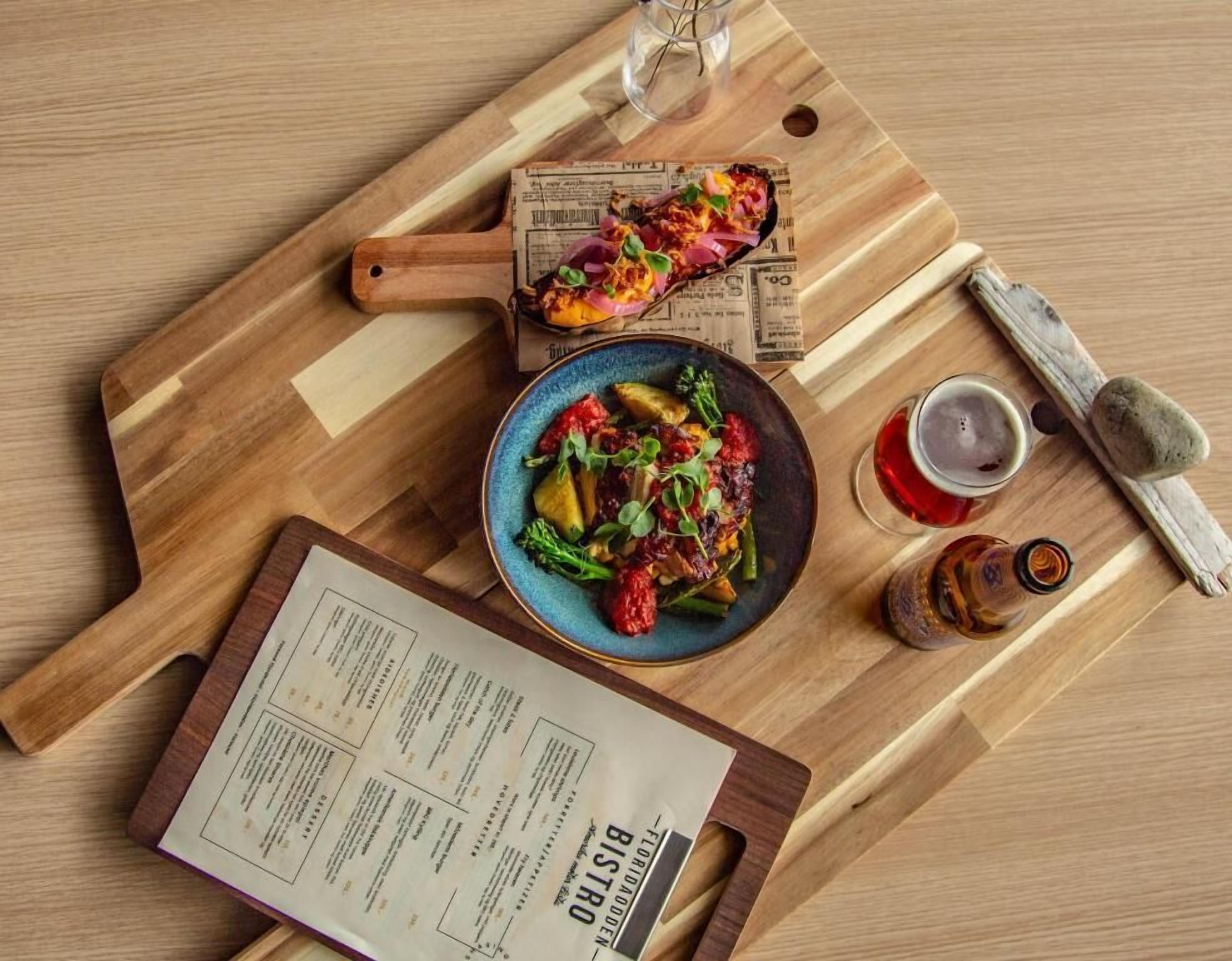 Una tabla de madera con un plato de comida, un menú y una botella de salsa.