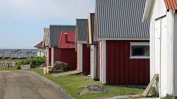 A row of red and white buildings with corrugated metal roofs, a gravel path, and a view of the sea in the background.