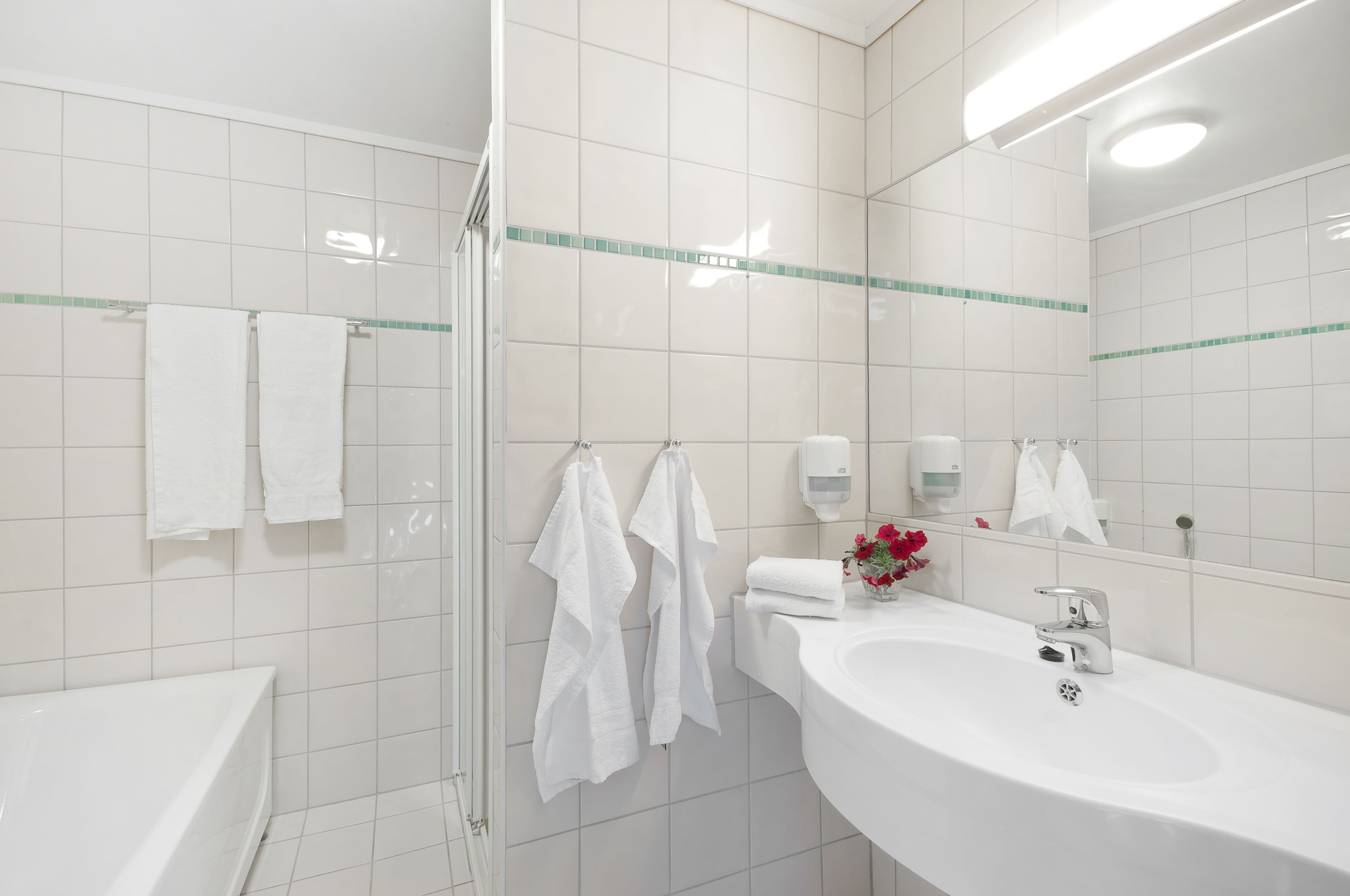 Een moderne badkamer met witte tegels, een douchecabine van glas, een wit wastafelmeubel met een kraan en een spiegel.
