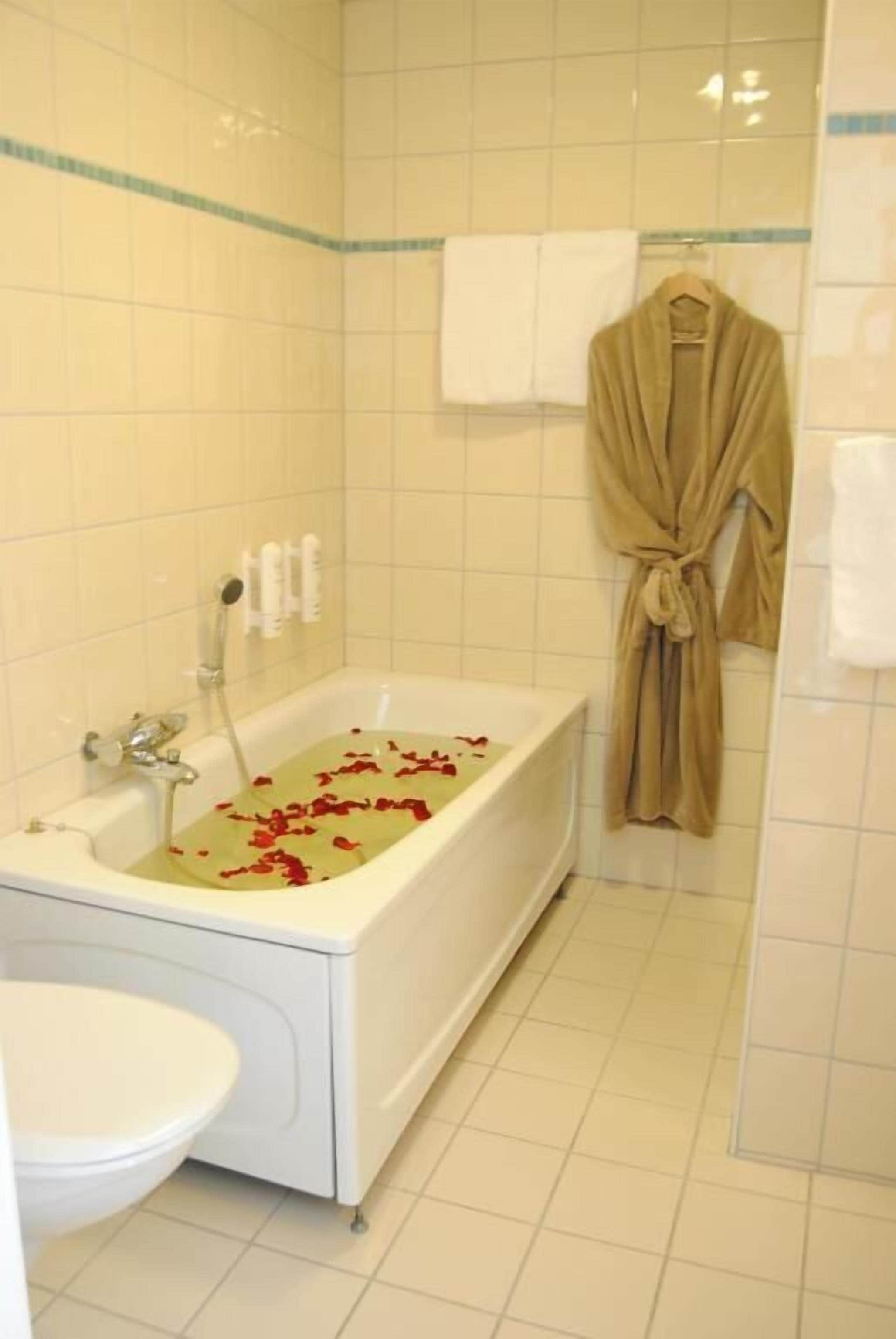 A bathroom with a bathtub filled with rose petals, a white sink, and a robe hanging on the wall.