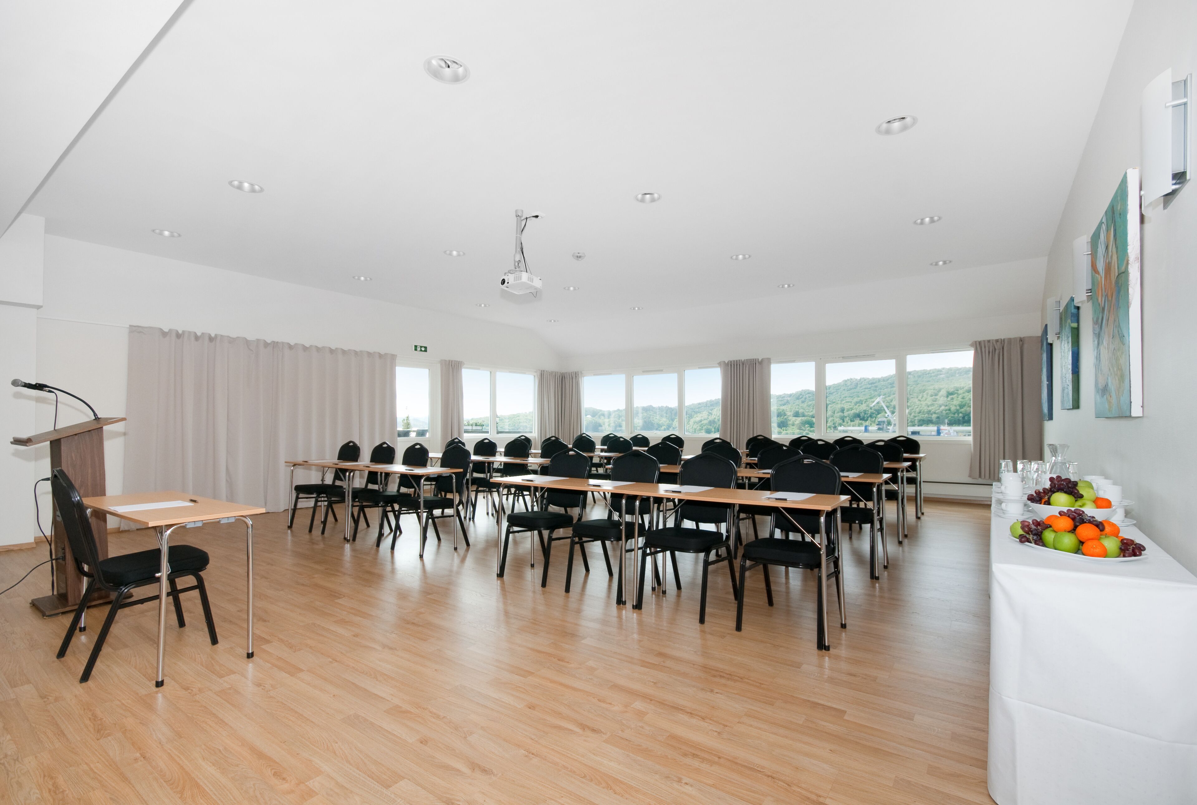 A conference room with a podium, rows of chairs, a table with fruits, and large windows with a view.