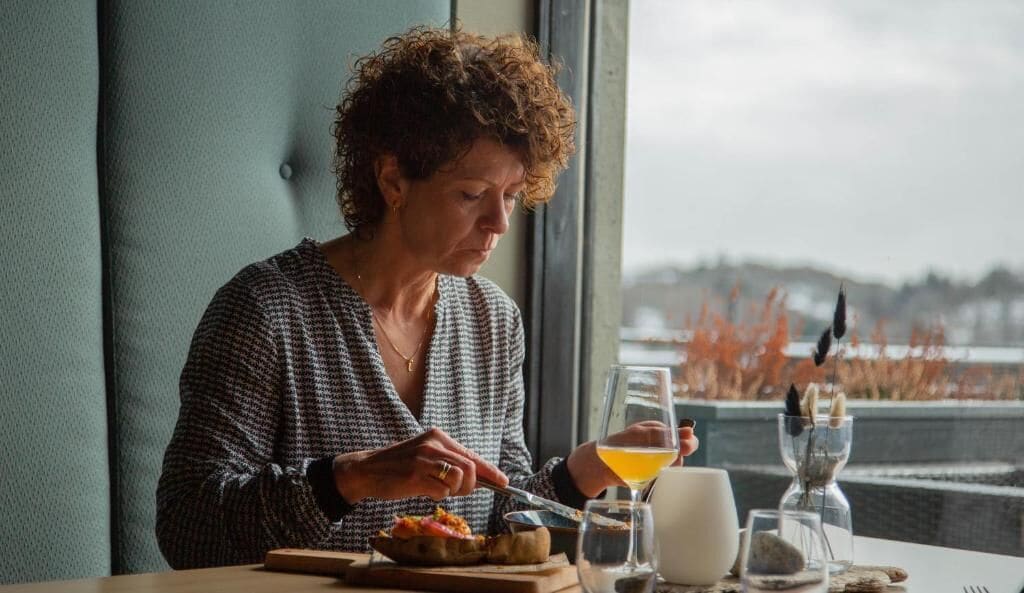 Una persona cenando en una mesa, con comida, bebida y vistas a un paisaje.